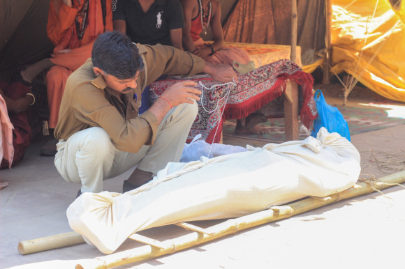 Un policía se encarga de coser la tela con la que envuelve el cuerpo de un hombre que minutos antes no hizo caso a quienes le avisaban que nadar en esa parte del Ganges era peligroso.